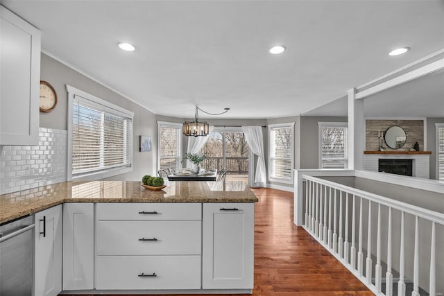 kitchen with a peninsula, a fireplace, dark wood-style floors, white cabinetry, and stainless steel dishwasher