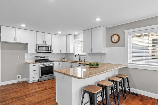 kitchen with white cabinetry, a peninsula, appliances with stainless steel finishes, and a sink