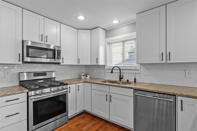 kitchen featuring a sink, wood finished floors, stainless steel appliances, white cabinets, and light stone countertops