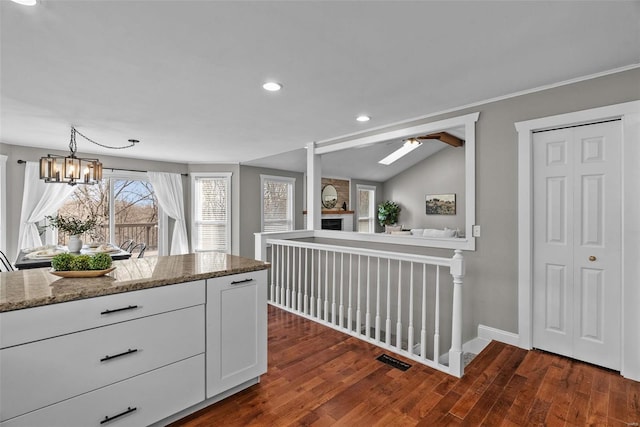 kitchen featuring visible vents, dark wood-type flooring, light stone counters, a fireplace, and white cabinets