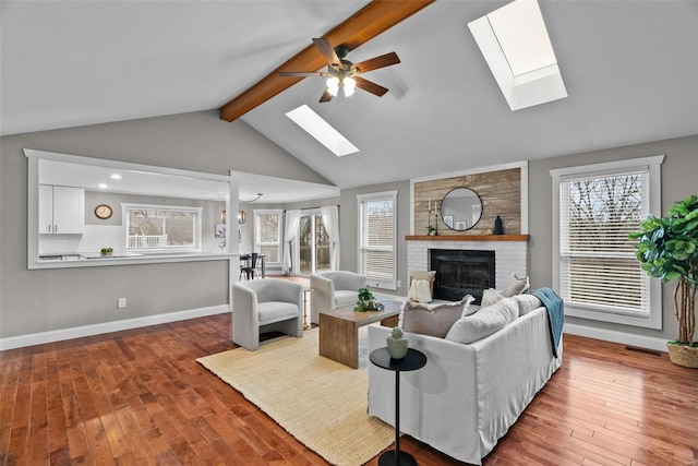 living room featuring baseboards, wood-type flooring, a brick fireplace, and vaulted ceiling with skylight