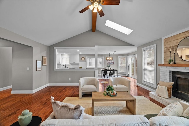 living room with baseboards, lofted ceiling with skylight, a brick fireplace, and wood finished floors