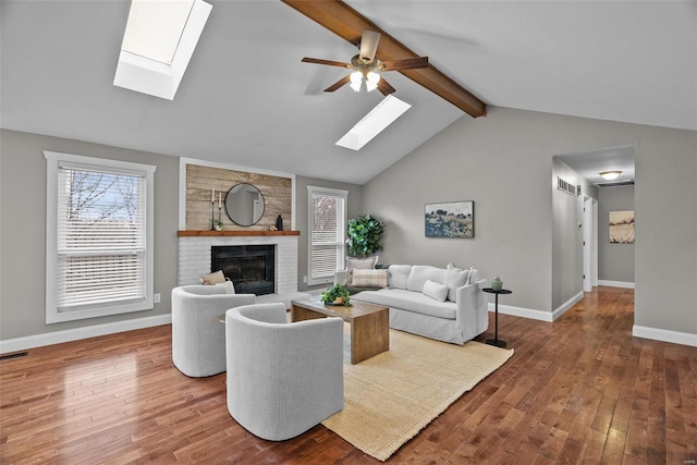 living area featuring hardwood / wood-style floors, a ceiling fan, baseboards, vaulted ceiling with beams, and a brick fireplace