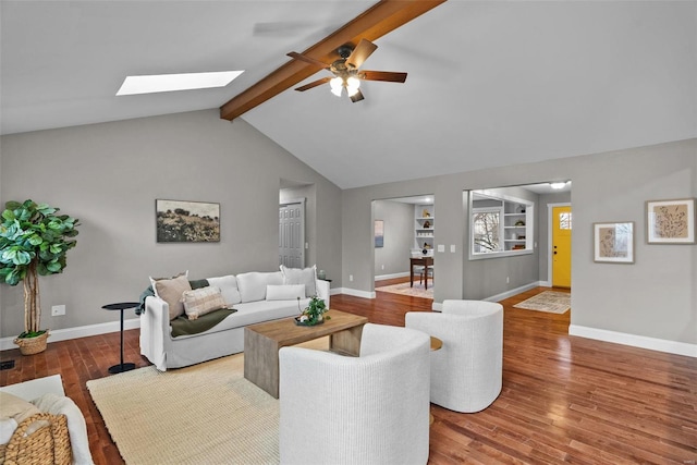 living area featuring built in shelves, baseboards, vaulted ceiling with skylight, wood finished floors, and a ceiling fan