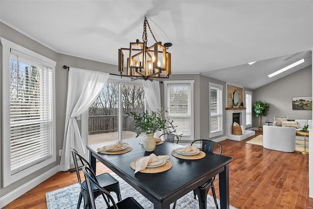 dining room with a healthy amount of sunlight, wood finished floors, a fireplace, and an inviting chandelier