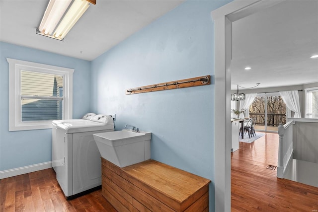 clothes washing area featuring a notable chandelier, washer and clothes dryer, a sink, wood finished floors, and laundry area