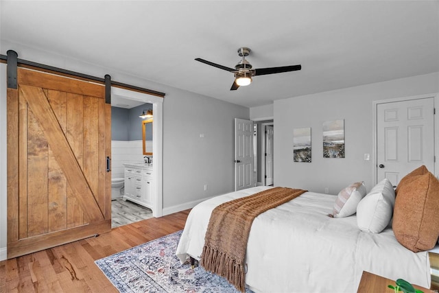 bedroom with a ceiling fan, light wood finished floors, a sink, ensuite bathroom, and a barn door