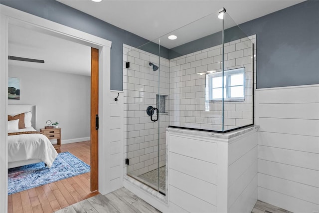 full bath featuring connected bathroom, wainscoting, wood finished floors, and a shower stall