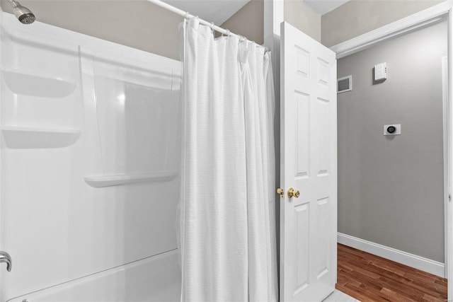 full bathroom with visible vents, wood finished floors, baseboards, and shower / tub combo with curtain