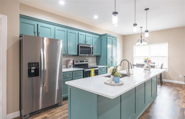 kitchen featuring dark wood-style floors, decorative light fixtures, light countertops, appliances with stainless steel finishes, and a kitchen island with sink