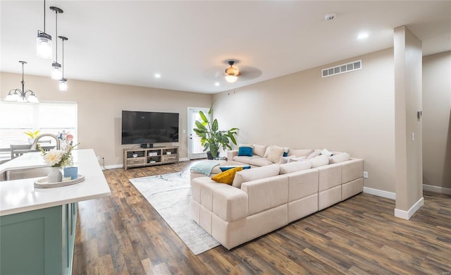 living room with dark wood-style floors, ceiling fan with notable chandelier, visible vents, and baseboards