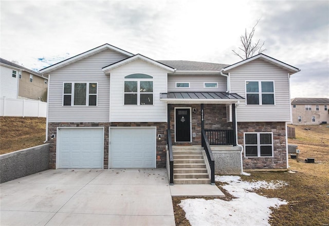 bi-level home with a garage, concrete driveway, stone siding, metal roof, and a standing seam roof