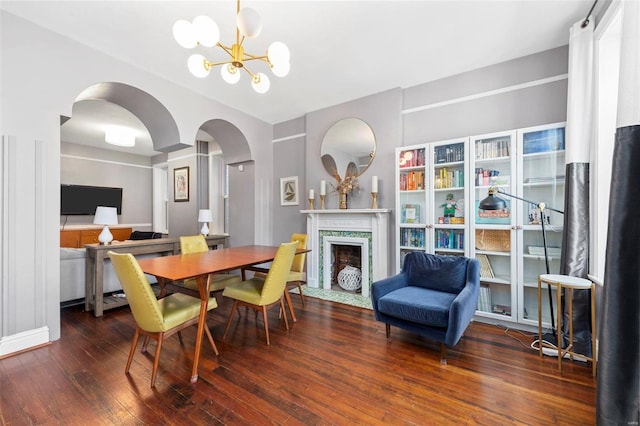 dining room with arched walkways, a fireplace, an inviting chandelier, and wood-type flooring