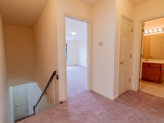 hallway featuring an upstairs landing, light carpet, and baseboards