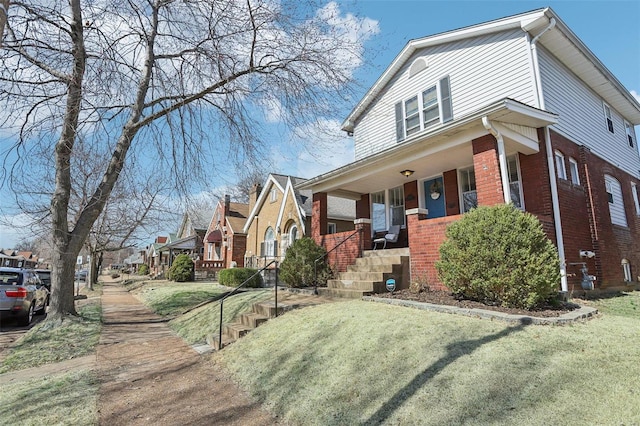 view of front of home featuring a porch, a front yard, brick siding, and a residential view