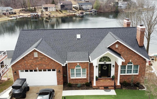 view of front facade with driveway, a chimney, an attached garage, a water view, and brick siding