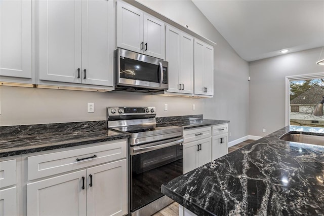 kitchen featuring lofted ceiling, appliances with stainless steel finishes, white cabinetry, dark stone countertops, and wood-type flooring