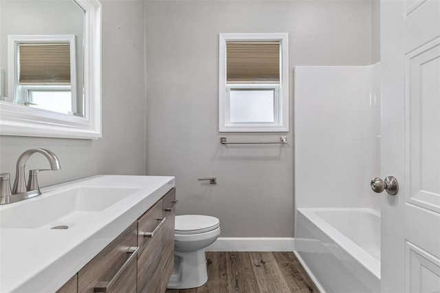 bathroom with wood-type flooring, a tub to relax in, vanity, and toilet