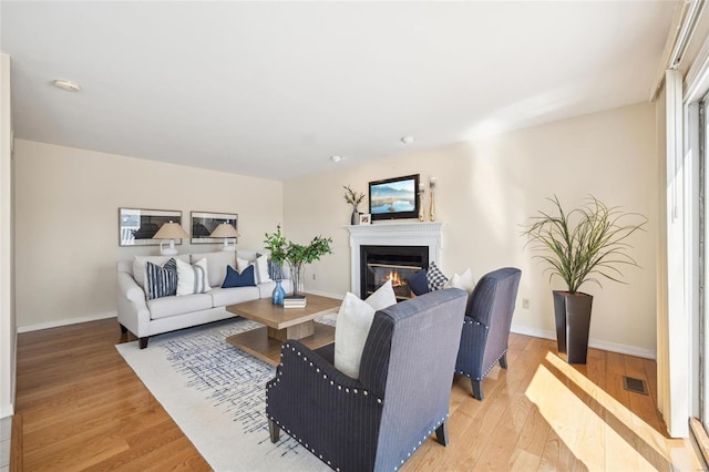 living area featuring light wood-type flooring, baseboards, visible vents, and a glass covered fireplace