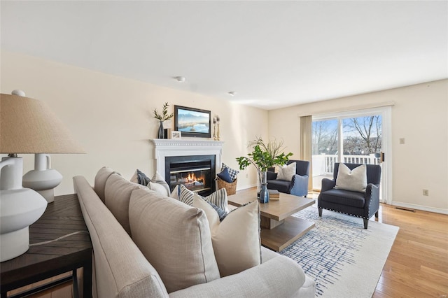 living room with light wood-type flooring, baseboards, visible vents, and a glass covered fireplace