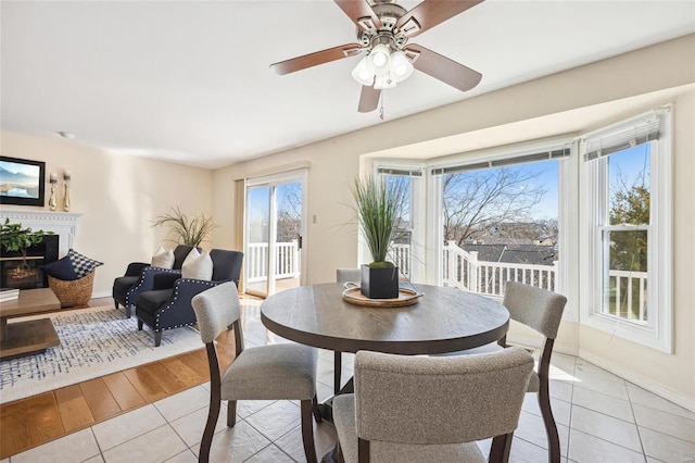 dining area with light tile patterned flooring, a glass covered fireplace, a ceiling fan, and baseboards