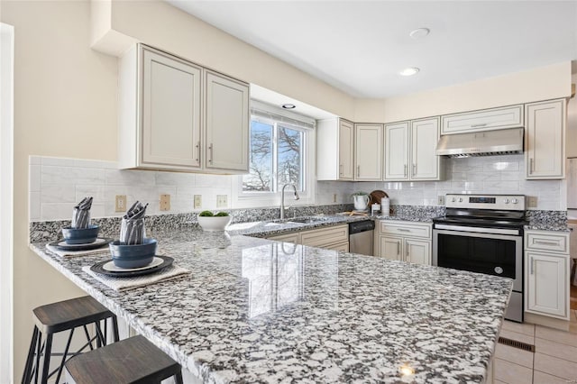 kitchen with under cabinet range hood, light stone counters, a sink, appliances with stainless steel finishes, and a peninsula