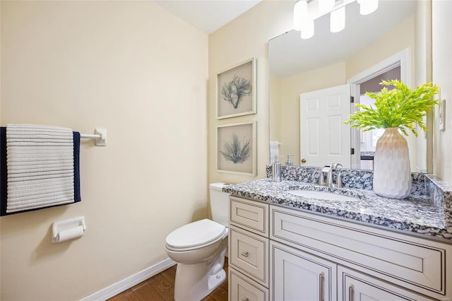 bathroom with vanity, toilet, wood finished floors, and baseboards