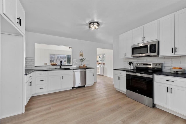 kitchen with a sink, dark countertops, light wood-style floors, and stainless steel appliances