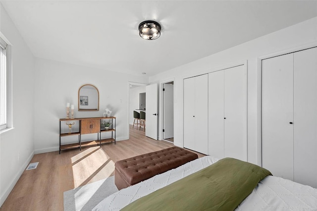 bedroom featuring visible vents, baseboards, multiple closets, and wood finished floors