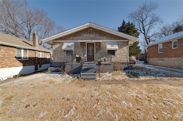 bungalow with stone siding, covered porch, and central air condition unit