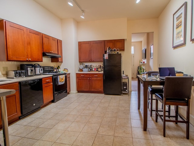 kitchen featuring under cabinet range hood, light countertops, light tile patterned flooring, brown cabinetry, and black appliances