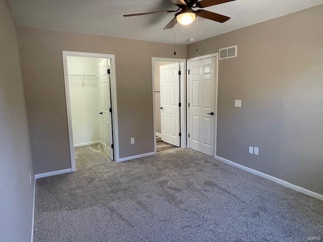 unfurnished bedroom featuring dark carpet, ceiling fan, a closet, and a walk in closet