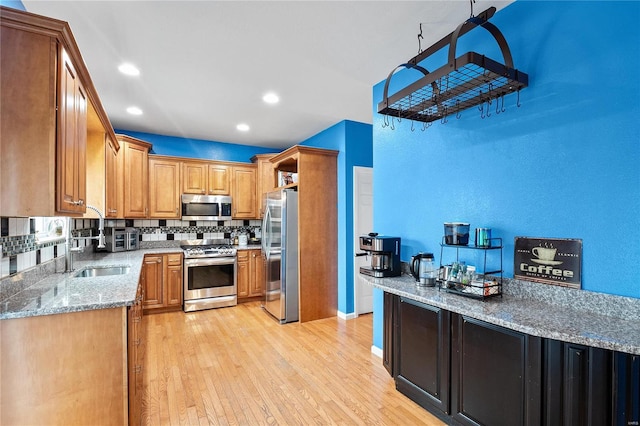 kitchen with stainless steel appliances, light wood-style floors, backsplash, light stone countertops, and brown cabinetry