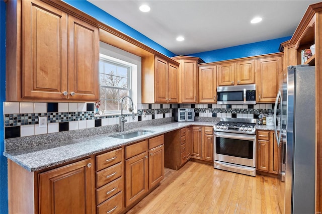 kitchen featuring light wood-style floors, appliances with stainless steel finishes, brown cabinetry, and a sink