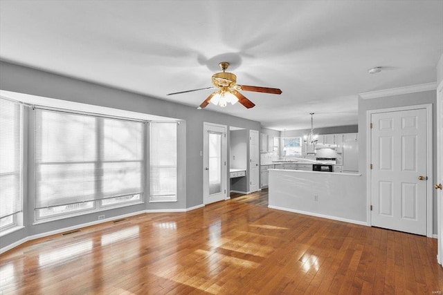 unfurnished living room featuring ceiling fan with notable chandelier, wood-type flooring, visible vents, and baseboards