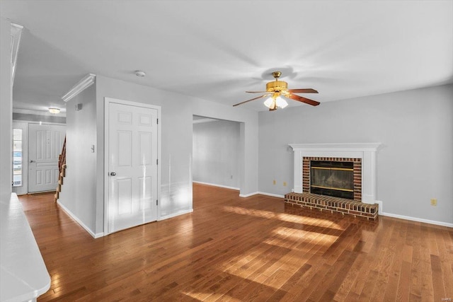 unfurnished living room featuring a ceiling fan, a brick fireplace, baseboards, and wood finished floors