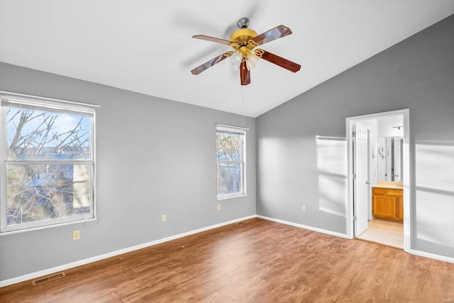 unfurnished bedroom with lofted ceiling, visible vents, baseboards, light wood finished floors, and ensuite bath