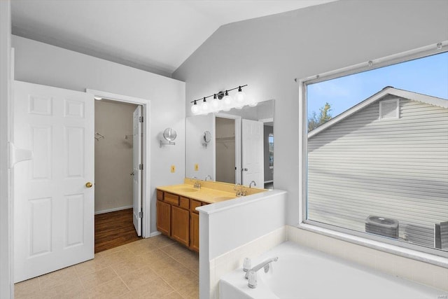 full bathroom featuring a walk in closet, a garden tub, vaulted ceiling, vanity, and tile patterned floors