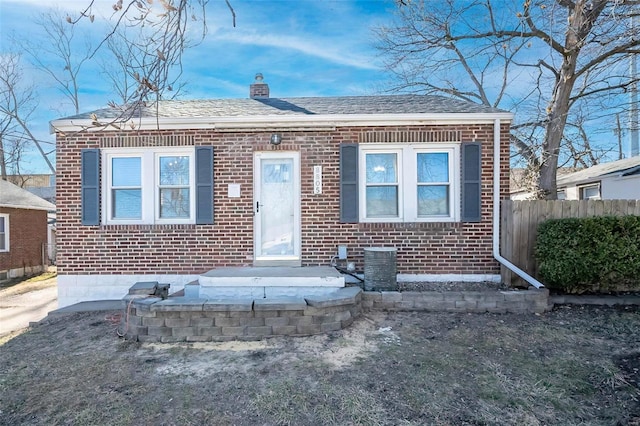 bungalow-style house with brick siding, a chimney, central AC unit, and fence