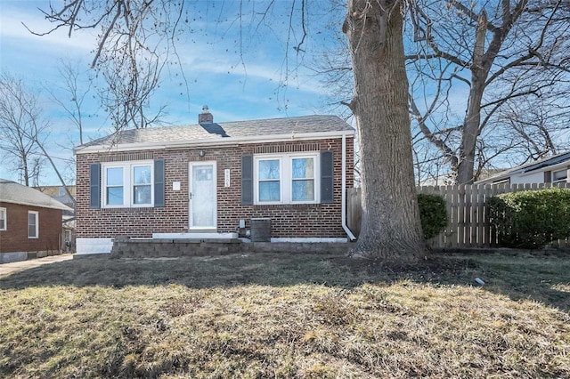 view of front of property featuring a front yard, a chimney, fence, and brick siding