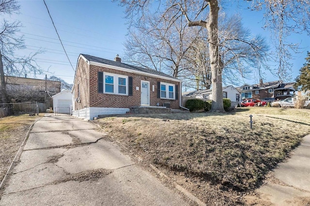 bungalow featuring an outbuilding, brick siding, a chimney, fence, and driveway