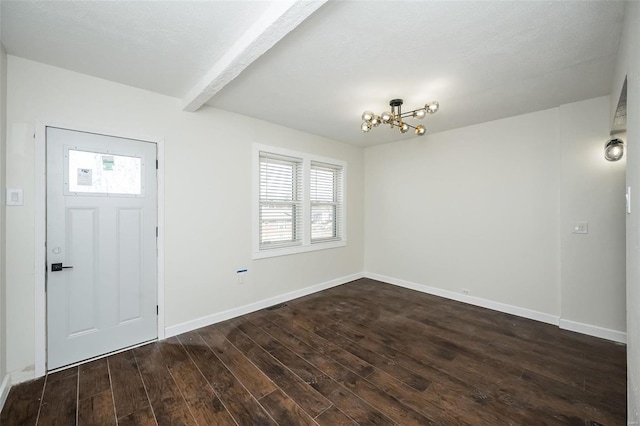 foyer entrance with a notable chandelier, beamed ceiling, dark wood finished floors, and baseboards