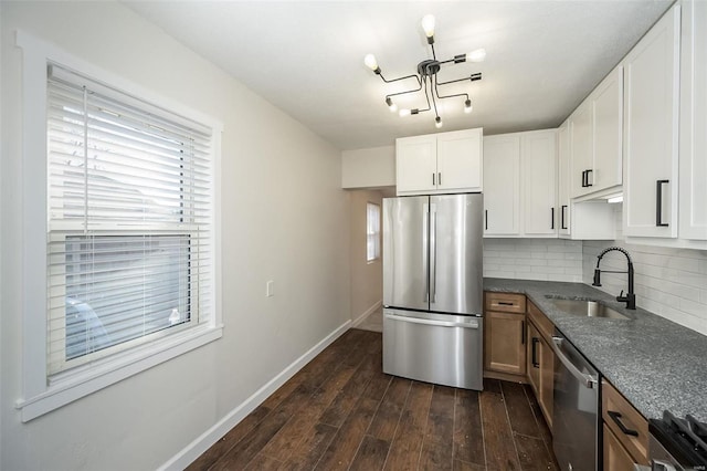 kitchen with baseboards, dark wood-type flooring, a sink, stainless steel appliances, and backsplash