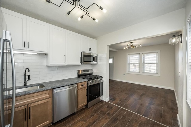 kitchen featuring dark wood-style flooring, dark countertops, backsplash, appliances with stainless steel finishes, and a sink