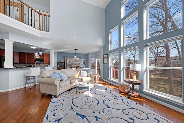 living room with baseboards, a chandelier, wood finished floors, and ornate columns