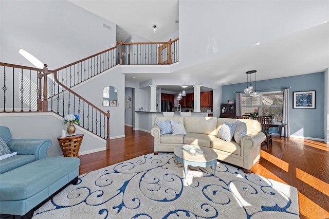 living area featuring ornate columns, visible vents, wood finished floors, baseboards, and stairs