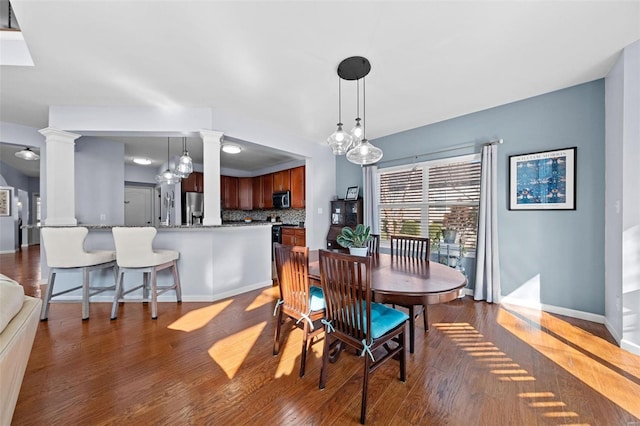 dining space featuring decorative columns, baseboards, and wood finished floors