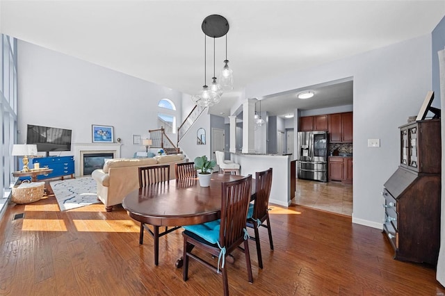 dining space with a glass covered fireplace, dark wood finished floors, stairway, and baseboards