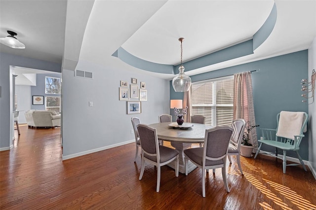 dining space featuring wood finished floors, a raised ceiling, visible vents, and baseboards