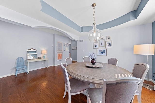 dining space with arched walkways, a tray ceiling, wood finished floors, and baseboards